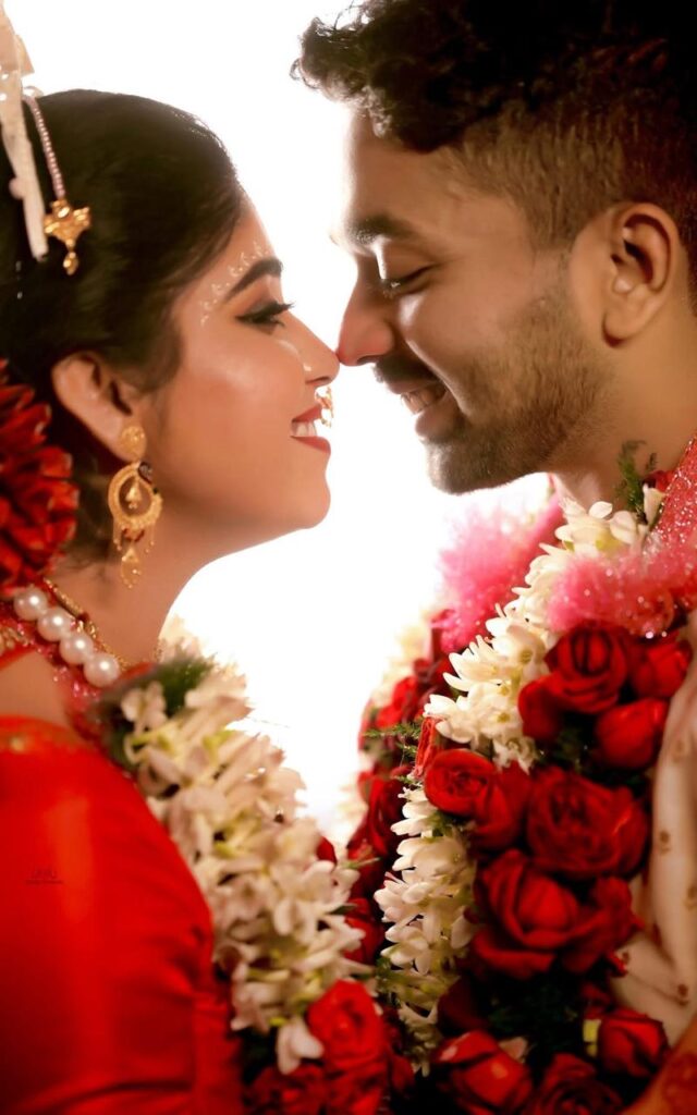 A close-up of a couple dressed in traditional wedding attire adorned with garlands, and a bride with a red veil displaying sindoor in her hair, symbolizing the sacred customs of a Hindu marriage ceremony.